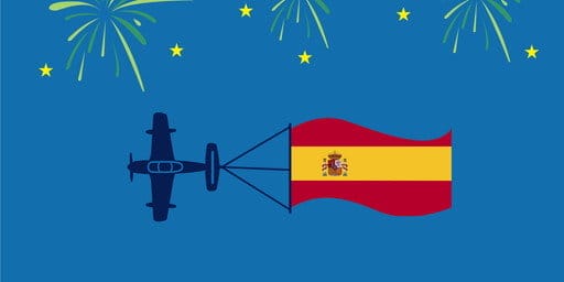 スペイン国の旗が描かれた飛行機が背景の上を飛び、花火が打ち上がる スペイン国の旗が描かれた飛行機が背景の上を飛び、花火が打ち上がる
