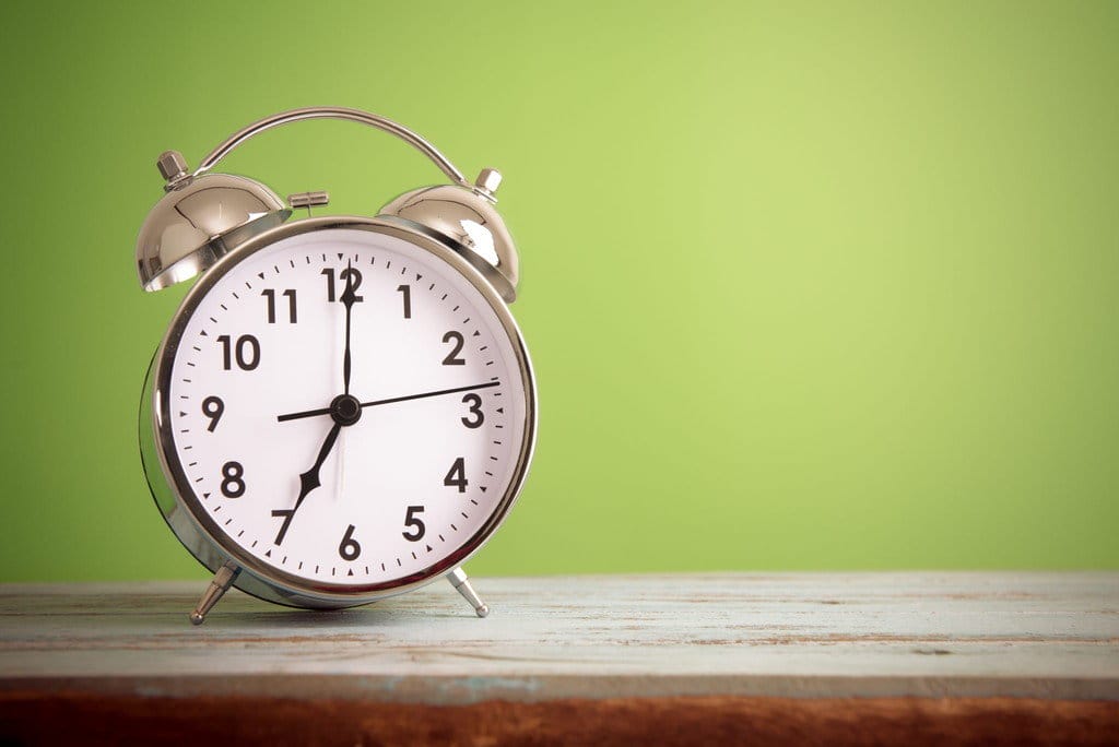 緑色の背景に木製のテーブルの上に置かれた目覚まし時計。スペイン風のアートワークが描かれています。 shutterstock_246286351