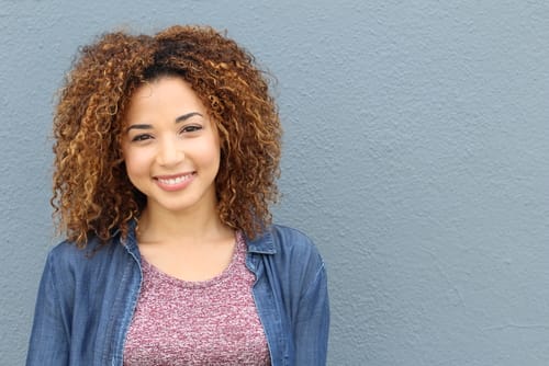 スペインの灰色の壁に向かって微笑む巻き毛の若い女性。