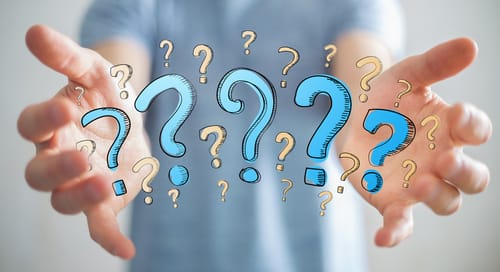 背景にスペイン国旗を掲げ、疑問符が付いた男性の手。