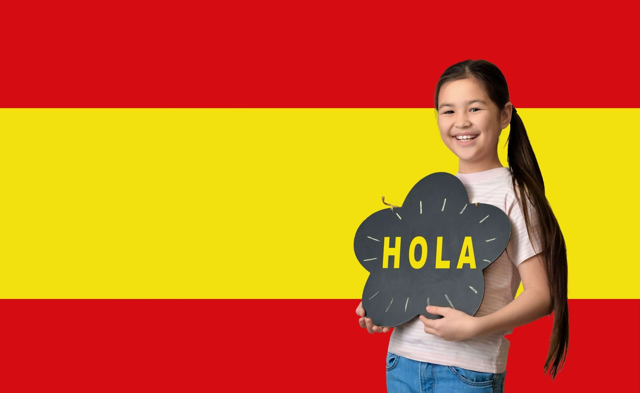 スペインの国旗の前で「hola」と書かれたプラカードを掲げ、スペイン語（スペイン語）を示す少女。