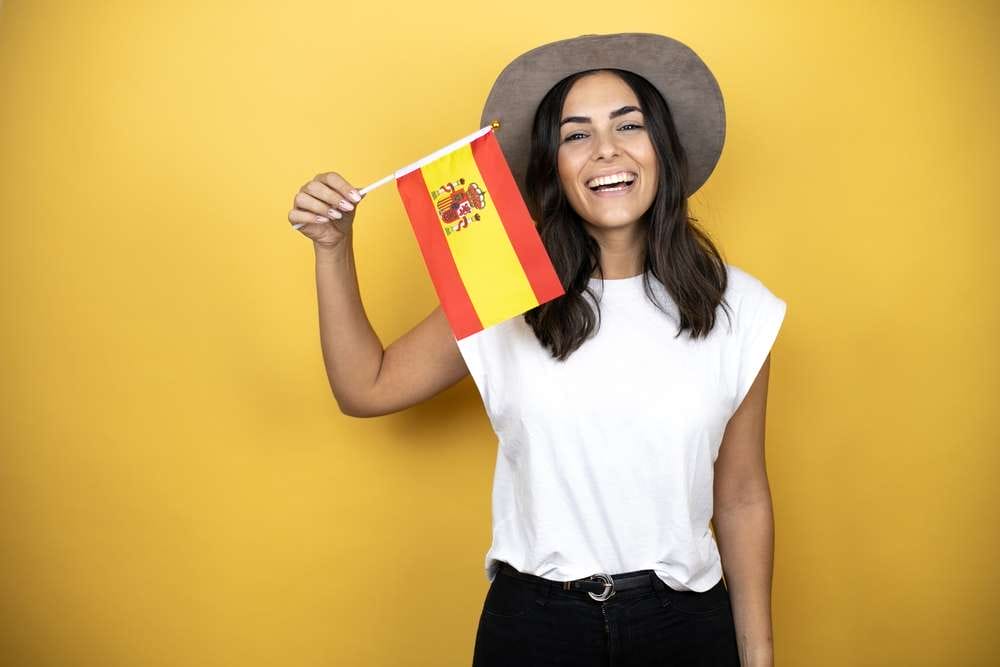 黄色の背景にスペインの国旗を持つ女性。 黄色の背景にスペインの国旗を持つ女性。